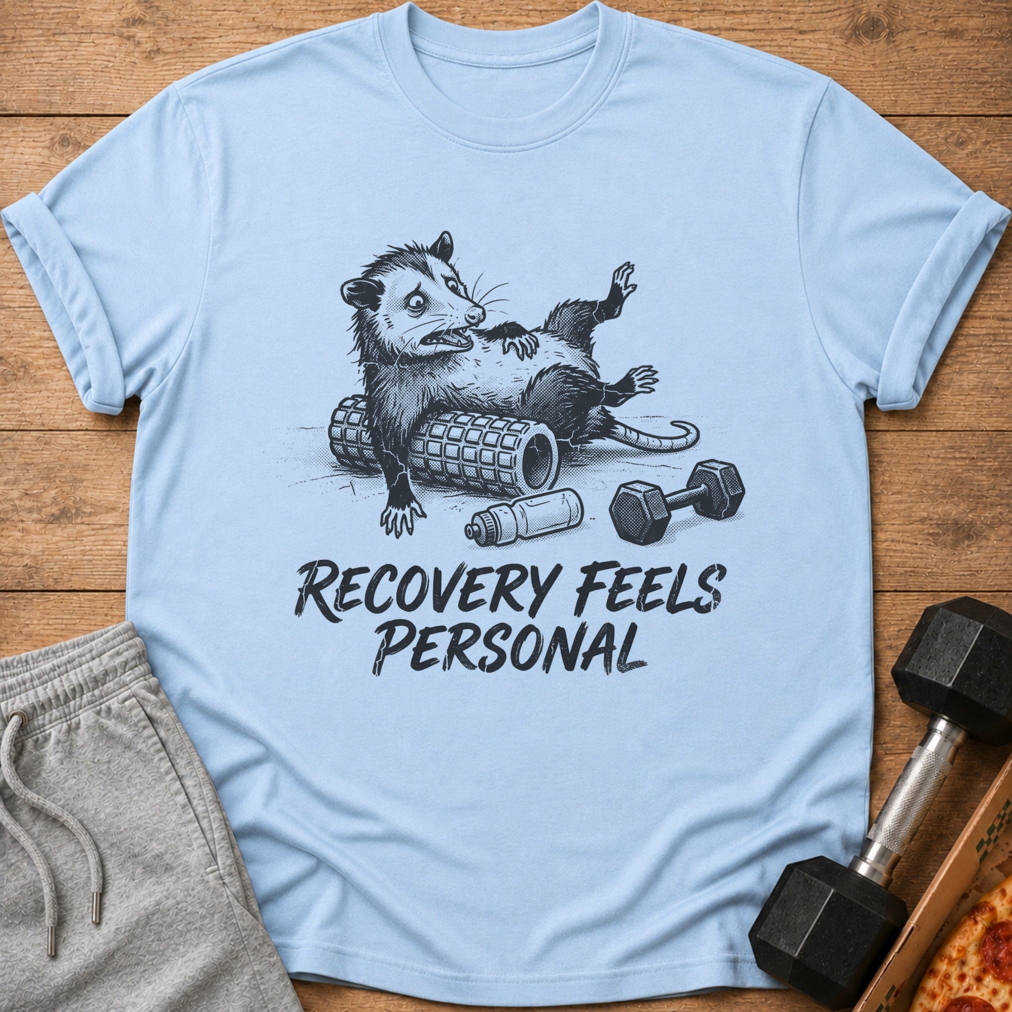 Opossum lying on a foam roller with a dumbbell and water bottle, text reads "Recovery Feels Personal".