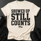Cream t-shirt with black distressed text "SHOWED UP STILL COUNTS" and a running shoe.