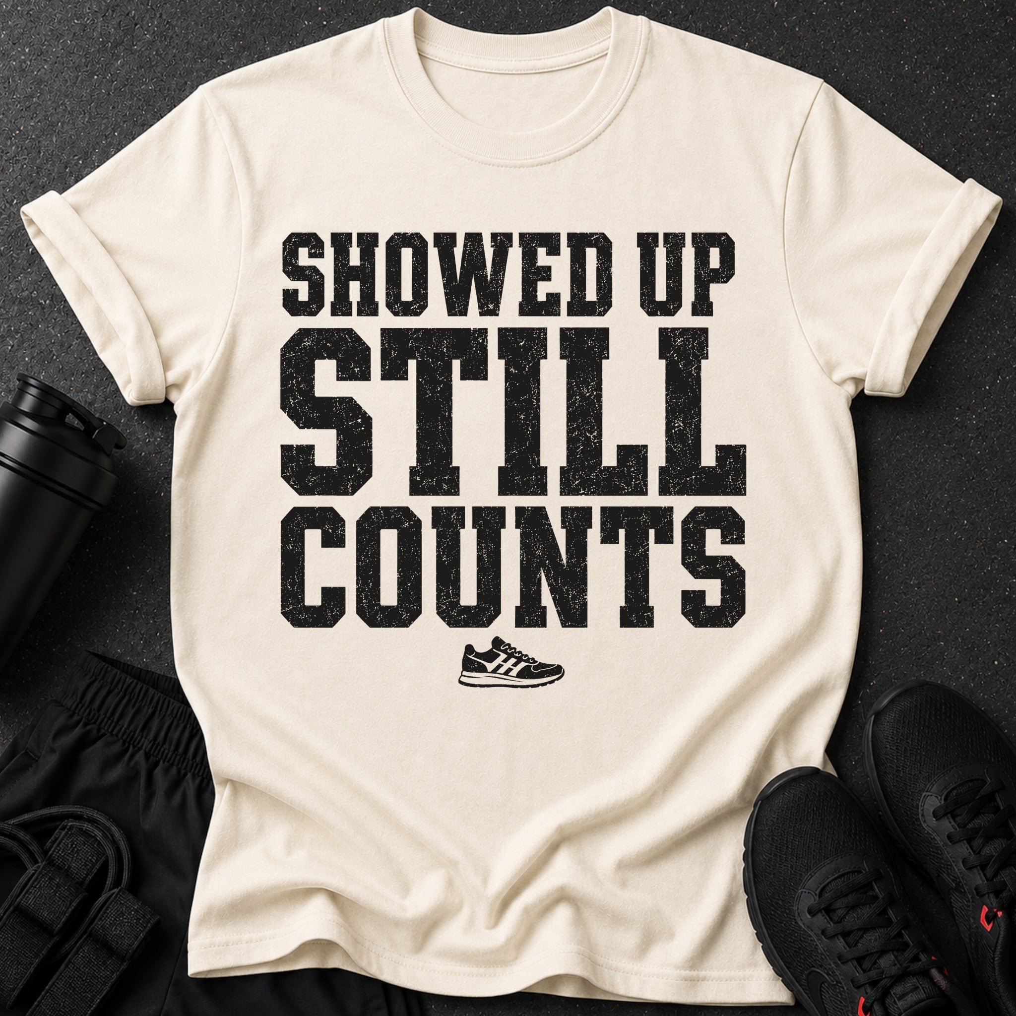 Cream t-shirt with black distressed text "SHOWED UP STILL COUNTS" and a running shoe.