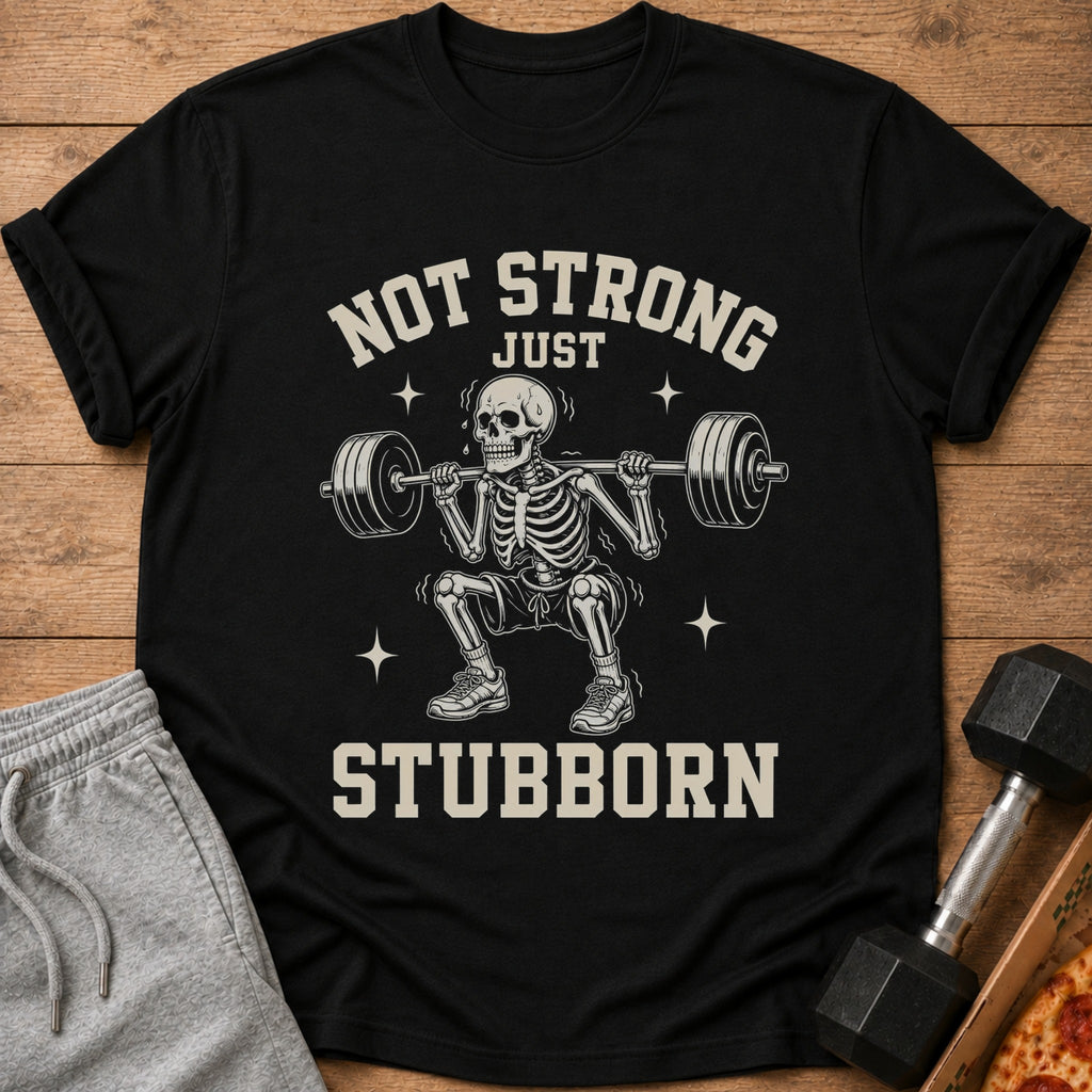 Black t-shirt with a skeleton lifting weights and text "NOT STRONG JUST STUBBORN".