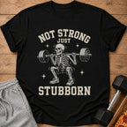 Black t-shirt with a skeleton lifting weights and text "NOT STRONG JUST STUBBORN".