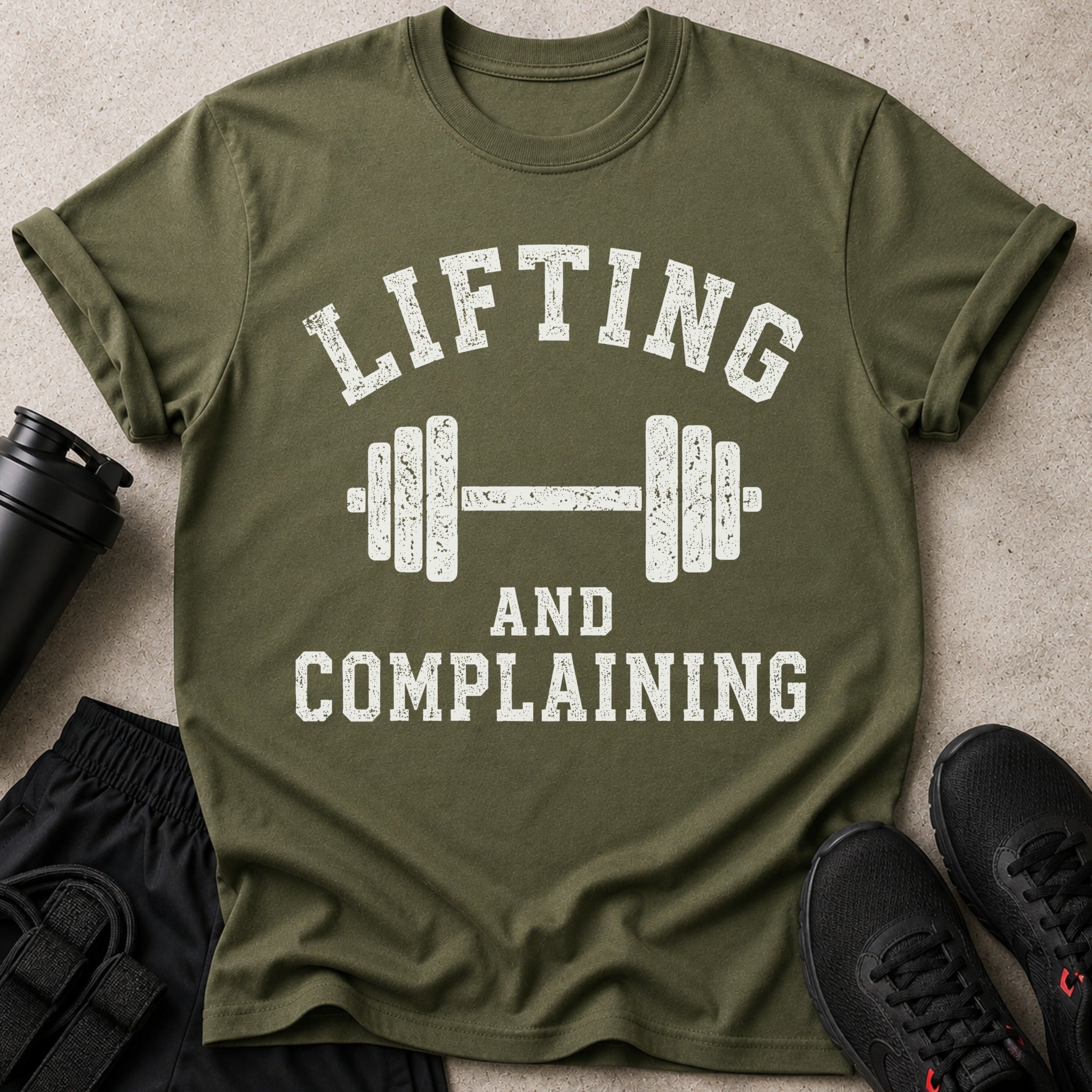 Olive green t-shirt with distressed white text "LIFTING AND COMPLAINING" and barbell graphic.