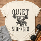 Cream t-shirt with black graphic of gorilla bench pressing and text "QUIET STRENGTH".