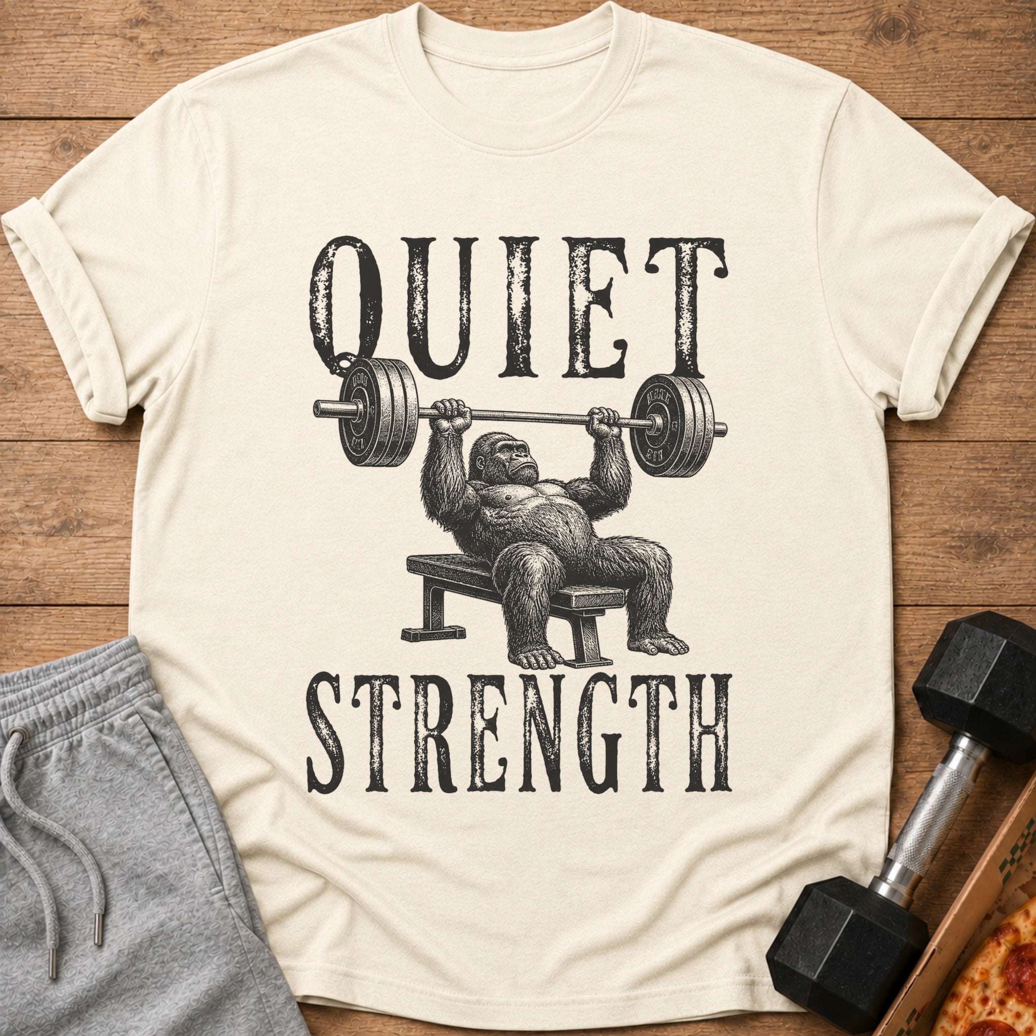 Cream t-shirt with black graphic of gorilla bench pressing and text "QUIET STRENGTH".