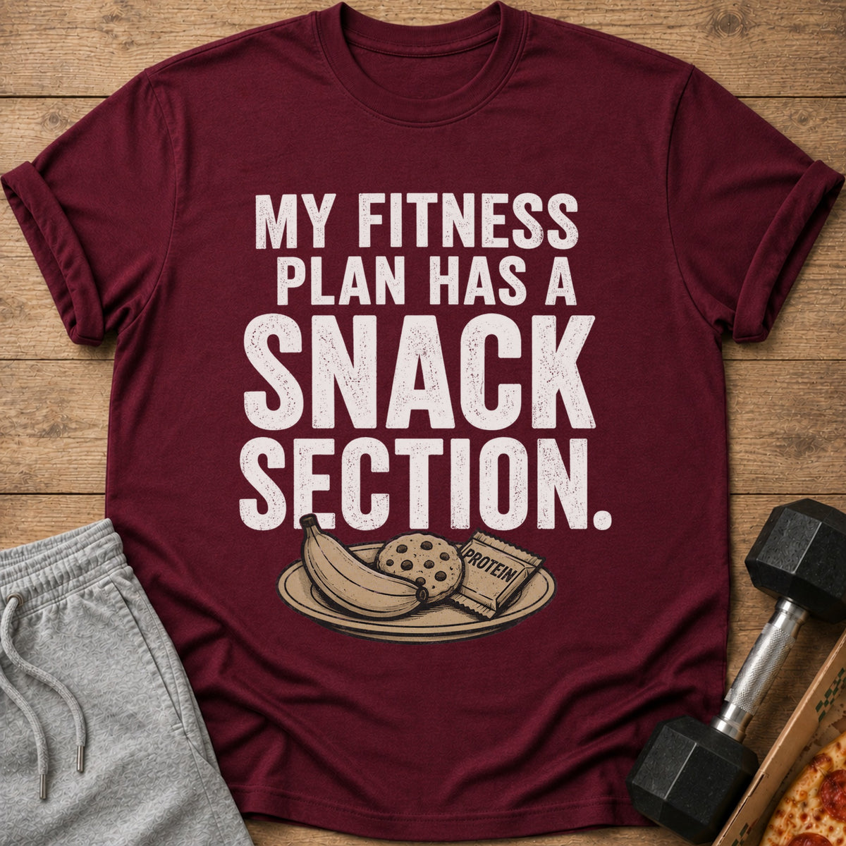 Maroon t-shirt with white text reading "MY FITNESS PLAN HAS A SNACK SECTION."