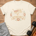 Cream t-shirt with a distressed graphic of a tired cat on a weight bench, text reads "Sore But Fine."