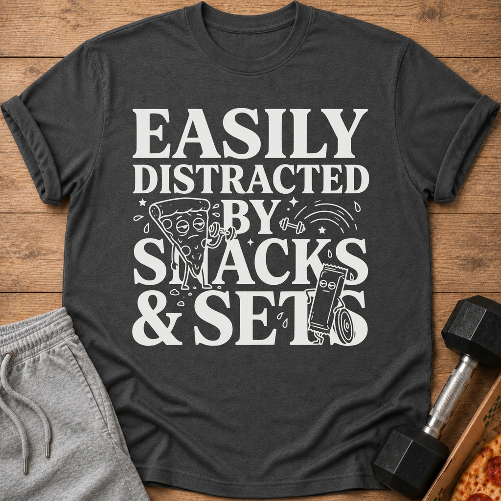 Dark gray t-shirt with white text "Easily Distracted By Snacks & Sets" and cartoon graphics.