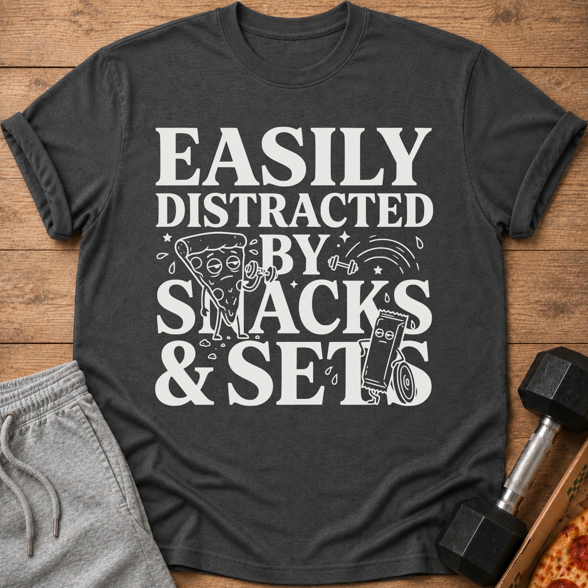 Dark gray t-shirt with white text "Easily Distracted By Snacks & Sets" and cartoon graphics.