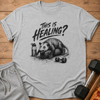 Opossum on foam roller with water bottle and dumbbell, "This Is Healing?" text.