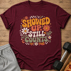 Maroon t-shirt with retro graphic "SHOWED UP STILL COUNTS" and floral accents.