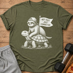 Sloth on turtle graphic with text "NOT FAST - JUST - COMMITTED" on olive t-shirt.