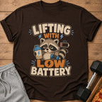T-shirt graphic of raccoon with dumbbell and protein shake, text reads "Lifting with Low Battery".