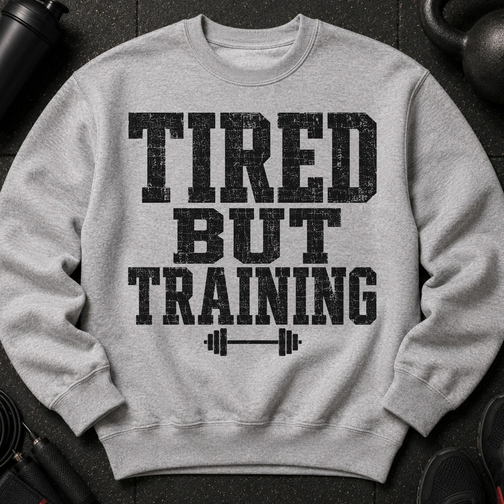 Gray sweatshirt with black distressed text "TIRED BUT TRAINING" and barbell graphic.