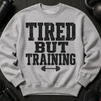 Gray sweatshirt with black distressed text "TIRED BUT TRAINING" and barbell graphic.