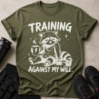 T-shirt with a raccoon drinking coffee, holding a dumbbell, and the text "TRAINING AGAINST MY WILL."