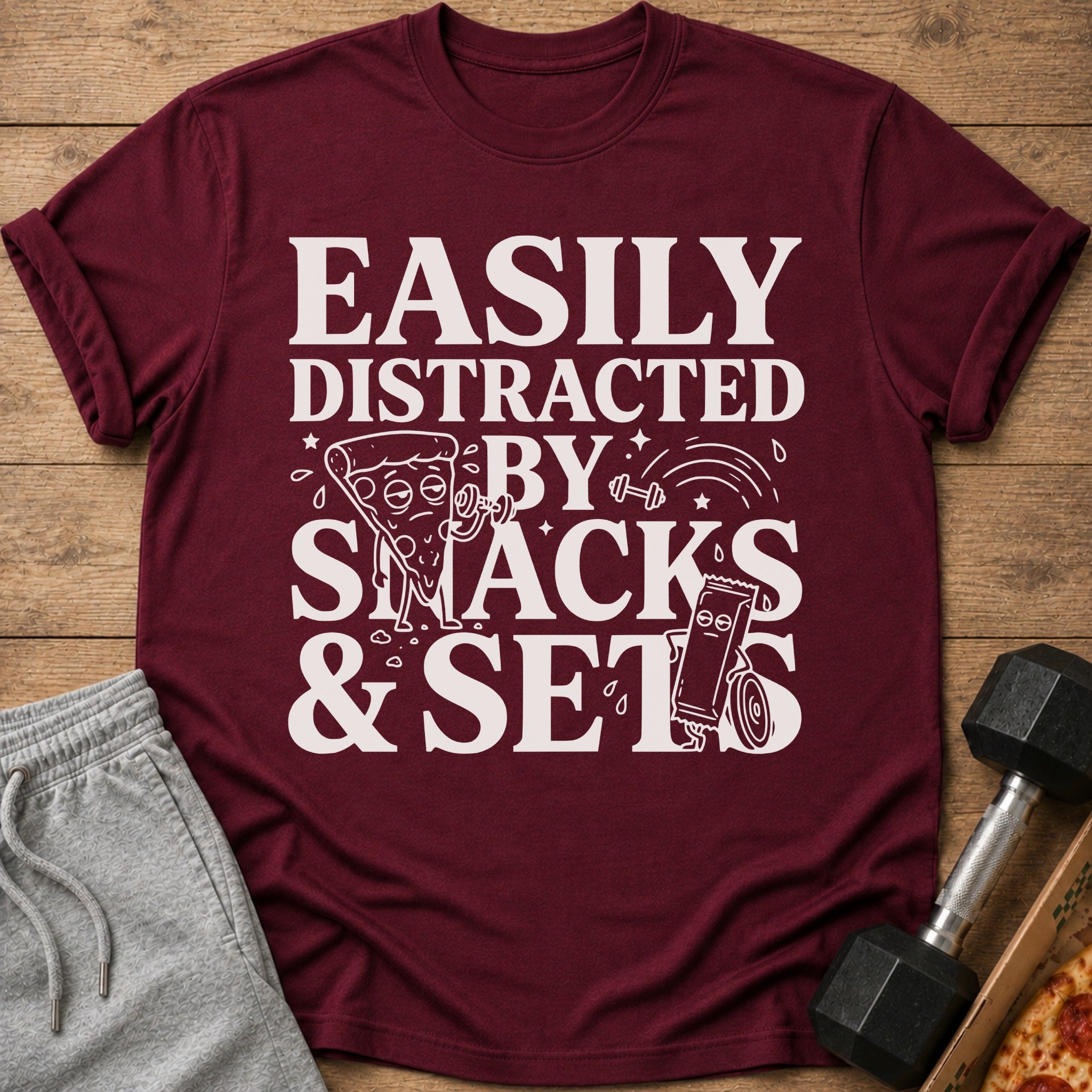 Maroon t-shirt with "Easily Distracted By Snacks & Sets" graphic featuring pizza and candy bar.