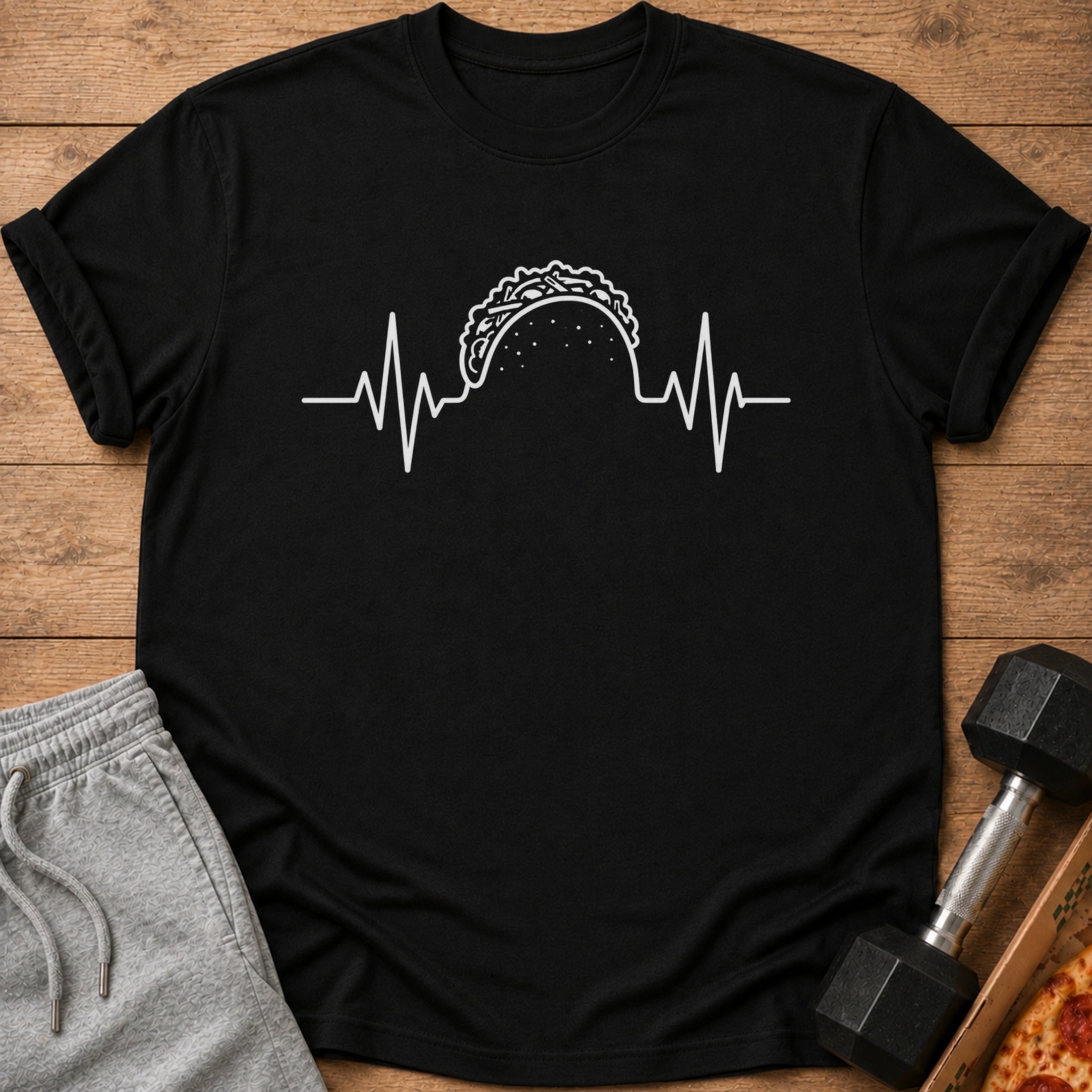 Black t-shirt with white taco heartbeat graphic, placed next to sweatpants and dumbbell.