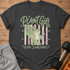 Charcoal gray t-shirt with a graphic of a frog holding a potted plant and a dumbbell, reading Plant Girl Gym Sometimes.