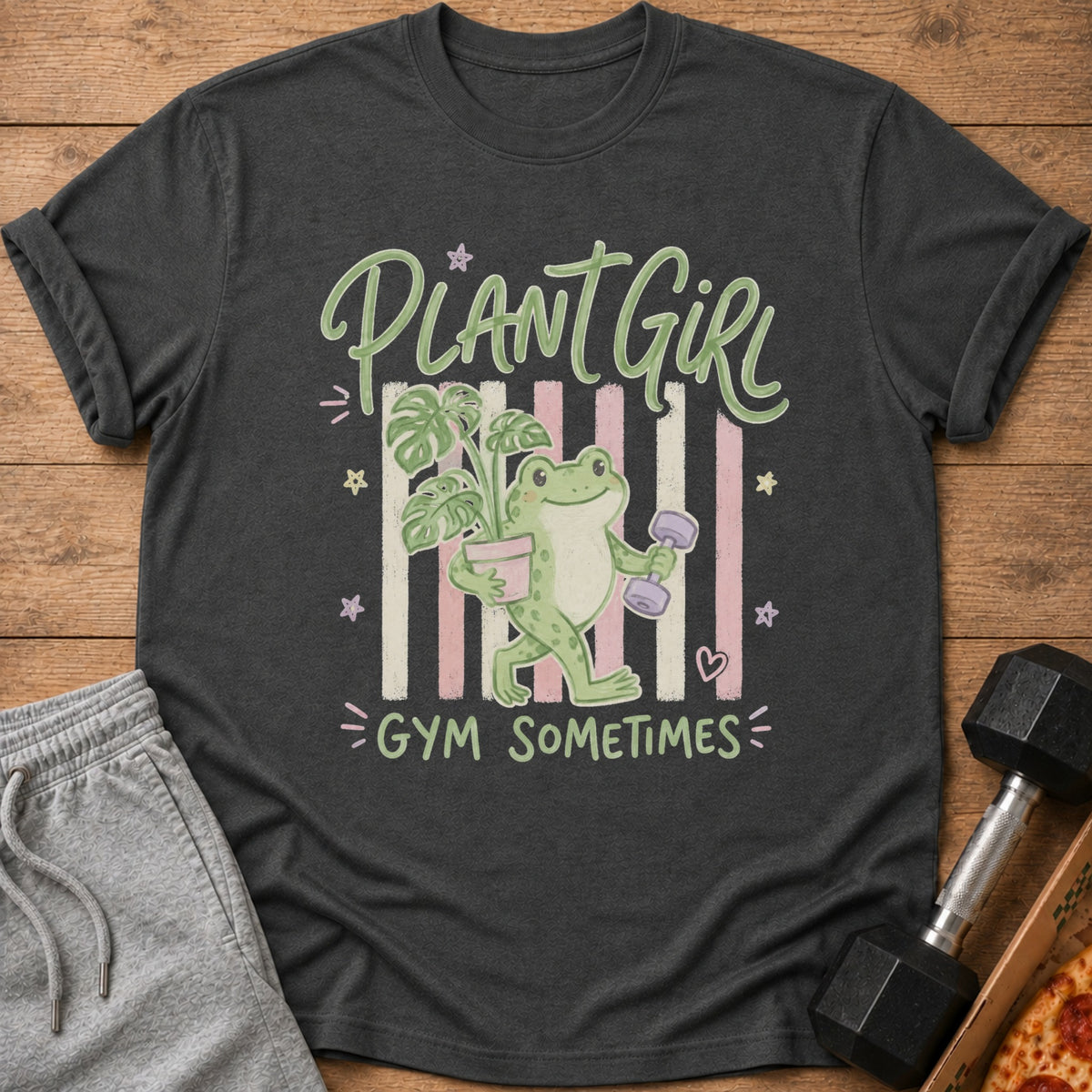 Charcoal gray t-shirt with a graphic of a frog holding a potted plant and a dumbbell, reading Plant Girl Gym Sometimes.
