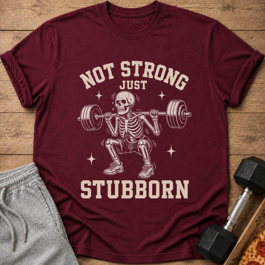 Maroon t-shirt with skeleton lifting weights and text "NOT STRONG JUST STUBBORN".
