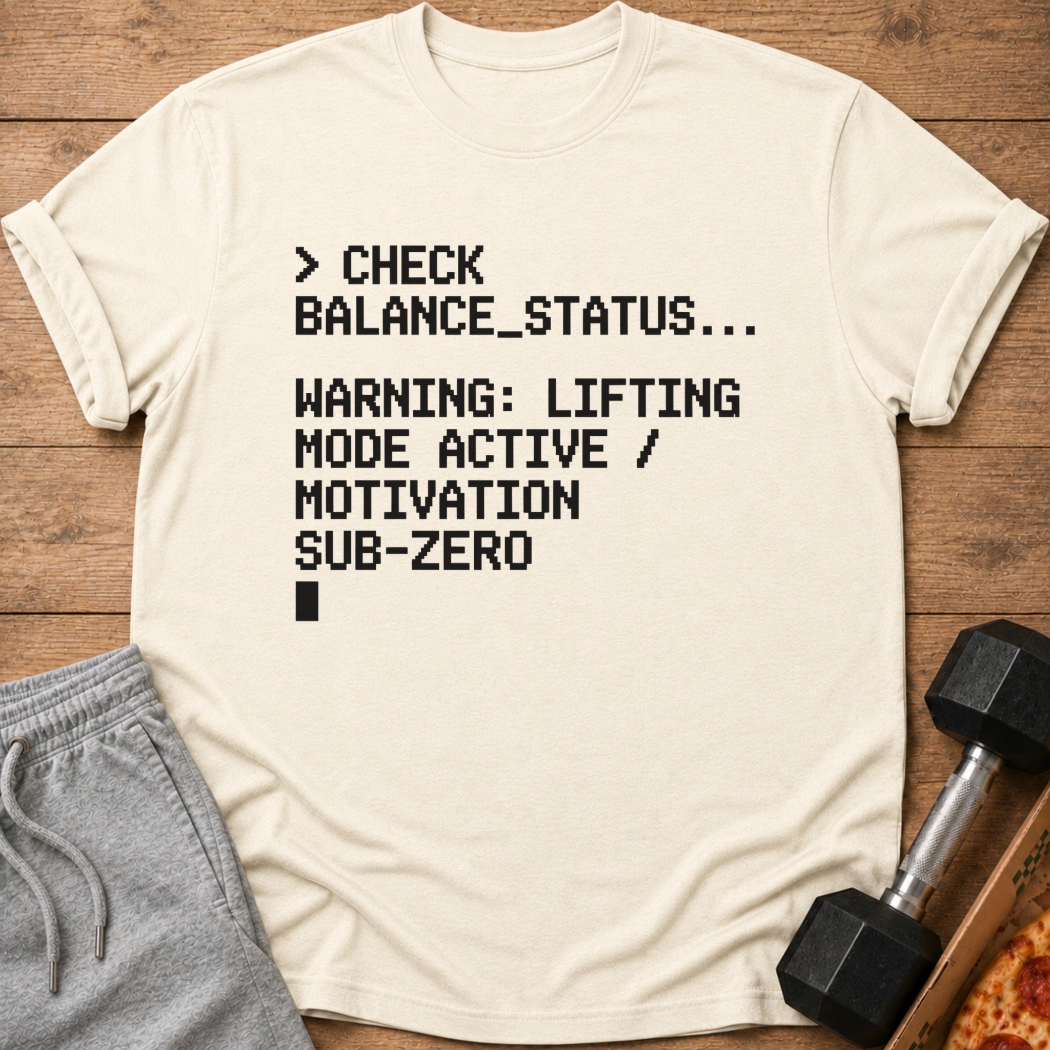 T-shirt with black pixelated text: CHECK BALANCE_STATUS, WARNING: LIFTING MODE ACTIVE / MOTIVATION SUB-ZERO.