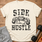 Crab lifting kettlebells with "SIDE HUSTLE" text on a cream t-shirt.