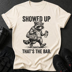Cream t-shirt with raccoon graphic and text "SHOWED UP THAT'S THE BAR."