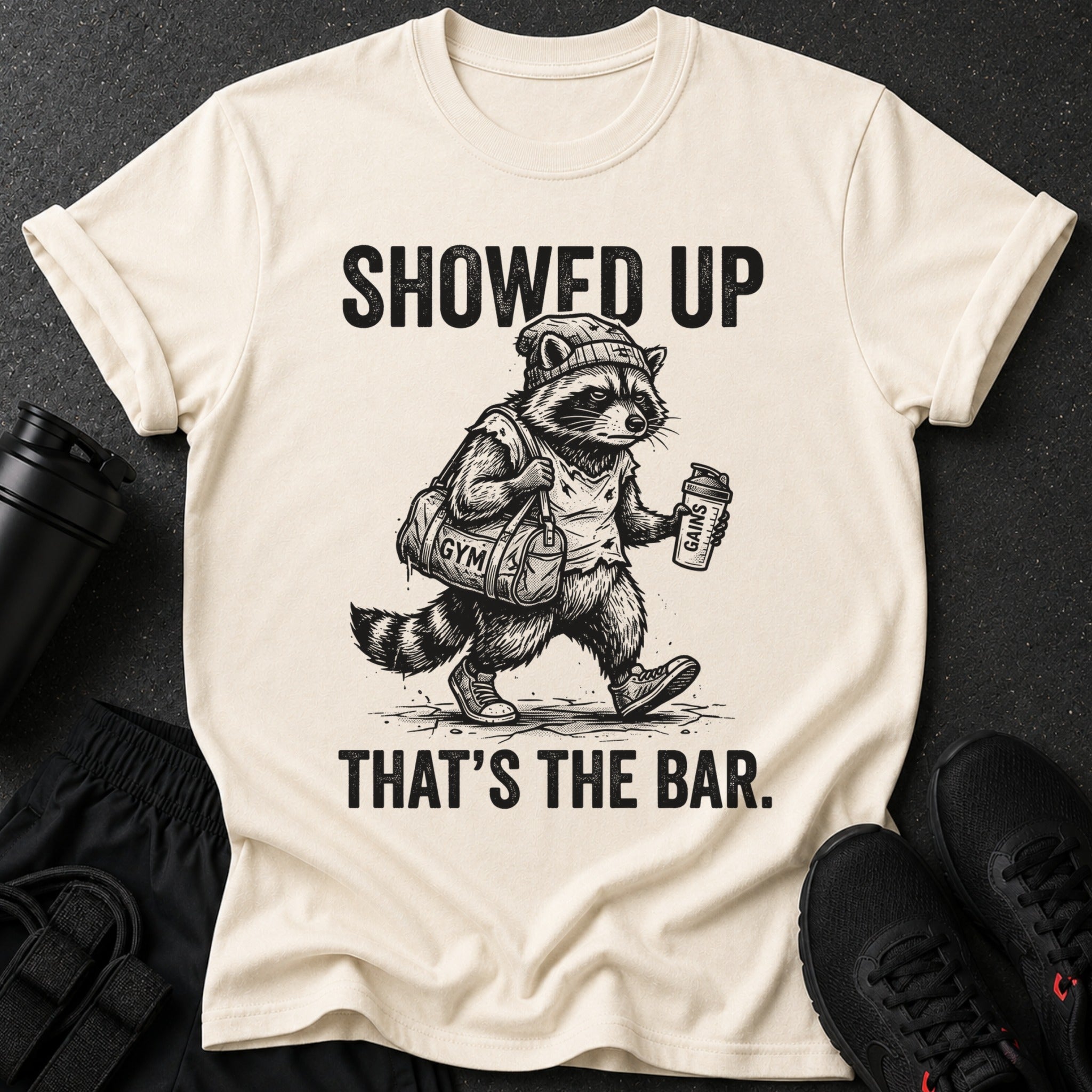 Cream t-shirt with raccoon graphic and text "SHOWED UP THAT'S THE BAR."