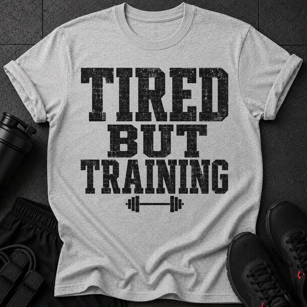 Grey t-shirt with black distressed text "TIRED BUT TRAINING" and barbell graphic.
