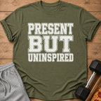 Olive green t-shirt with "PRESENT BUT UNINSPIRED" text and gym accessories.