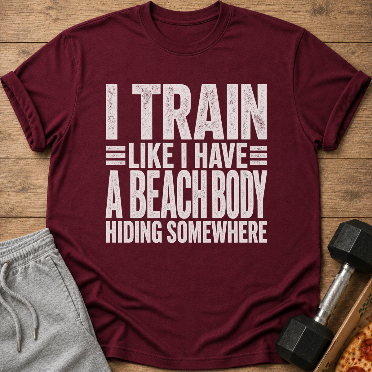 Maroon t-shirt with text "I TRAIN LIKE I HAVE A BEACH BODY HIDING SOMEWHERE".