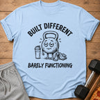 Light blue t-shirt with cartoon kettlebell saying "BUILT DIFFERENT BARELY FUNCTIONING".