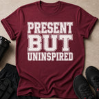 Maroon t-shirt with white distressed text reading "PRESENT BUT UNINSPIRED".