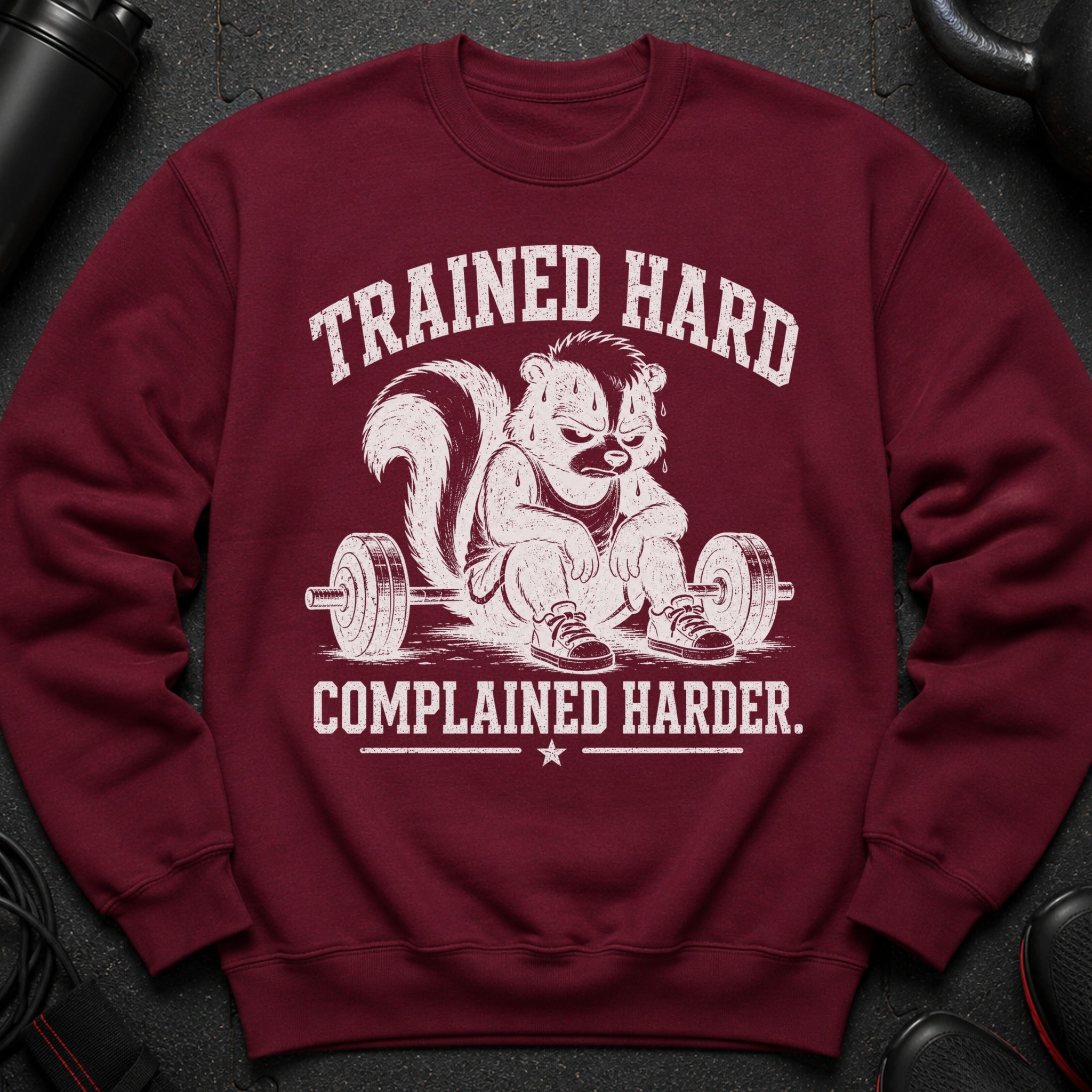 Maroon sweatshirt with skunk drawing and text: "Trained Hard, Complained Harder."