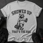 Grey t-shirt with a raccoon graphic, saying "SHOWED UP DONE THAT'S THE BAR."