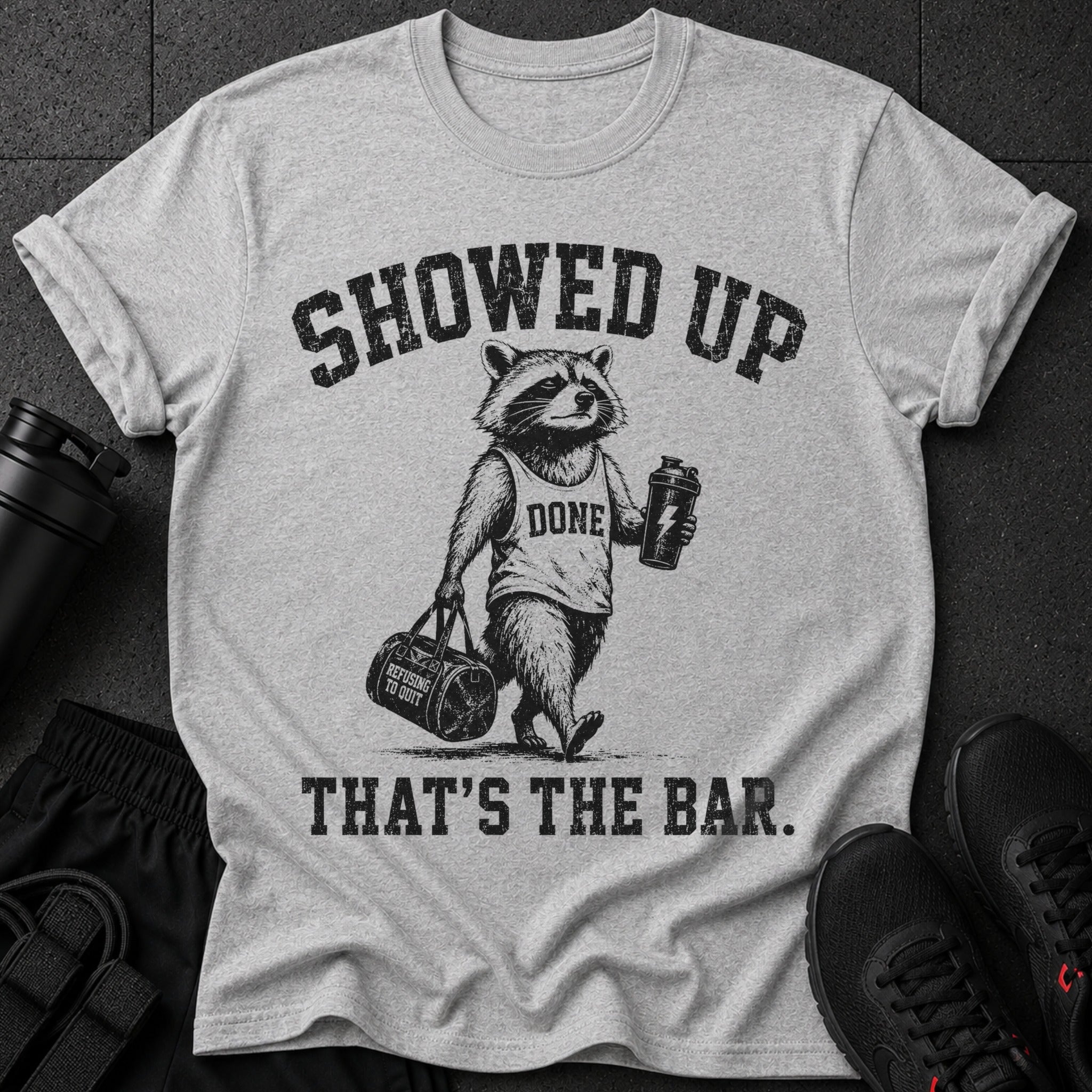 Grey t-shirt with a raccoon graphic, saying "SHOWED UP DONE THAT'S THE BAR."
