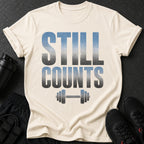 Cream t-shirt with "STILL COUNTS" text and dumbbell graphic.