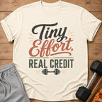 Cream t-shirt with text "Tiny Effort, Real Credit" and dumbbell graphic.