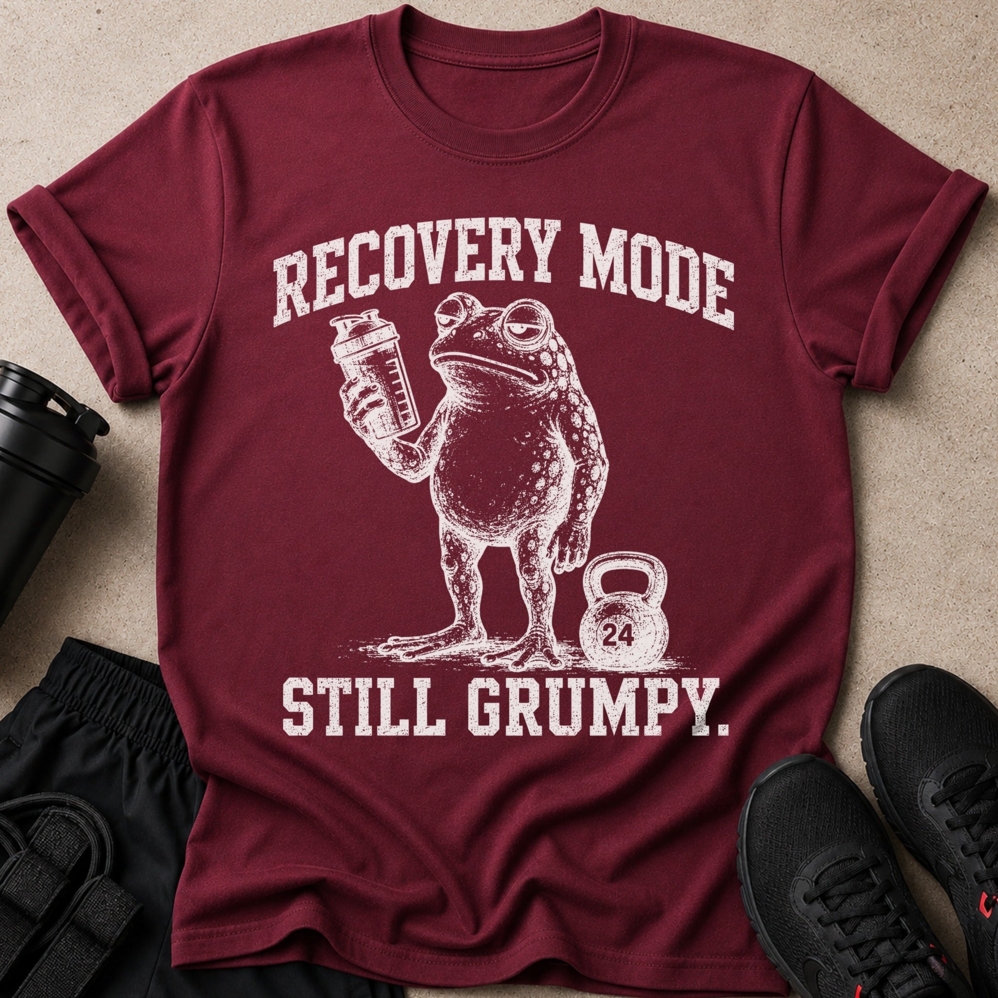 Maroon t-shirt with distressed print of a grumpy frog holding a shaker bottle and a kettlebell.