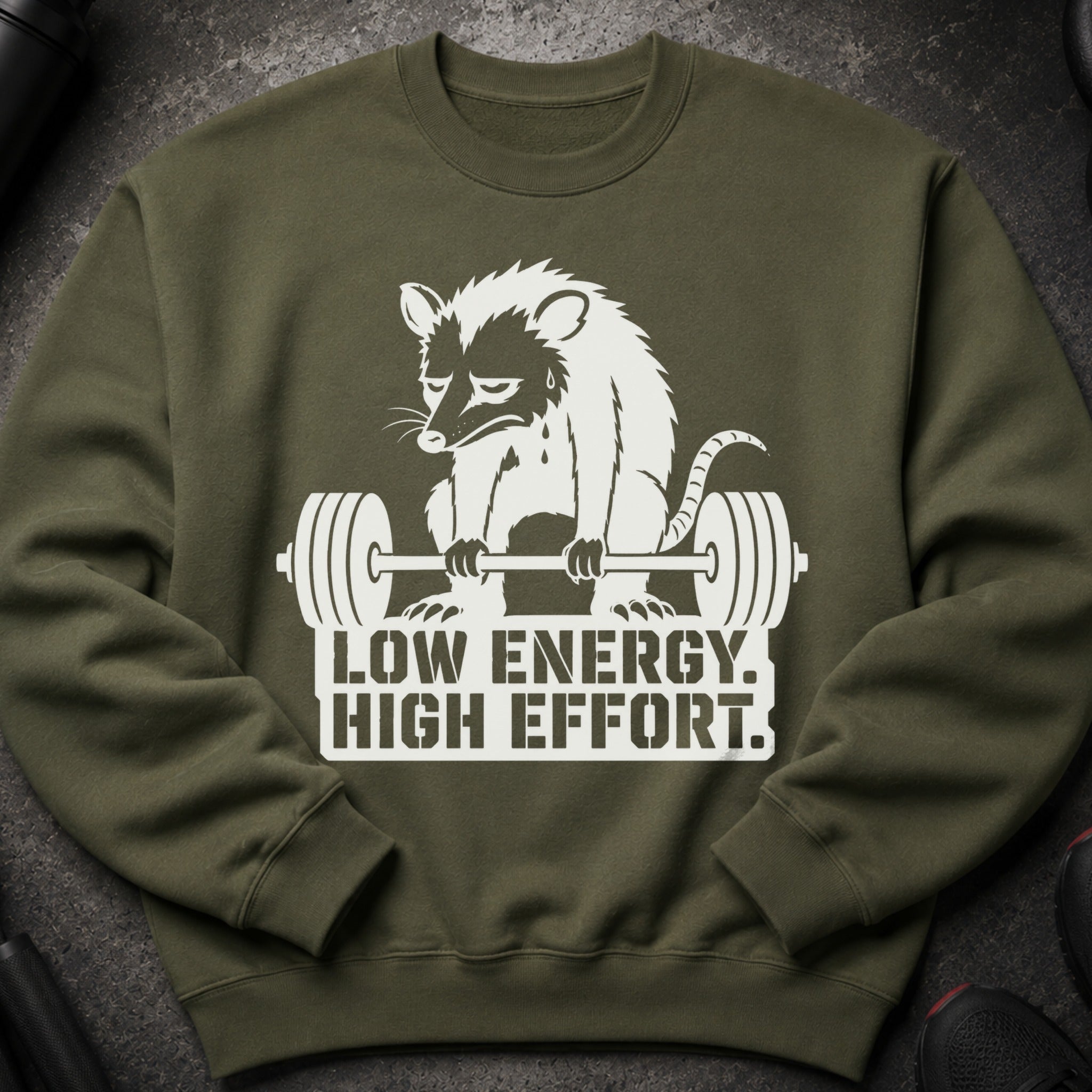 Olive green sweatshirt with a white graphic of a struggling opossum lifting weights and text.