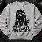Raccoon lifting weights with "RARELY MOTIVATED" text on gray sweatshirt.