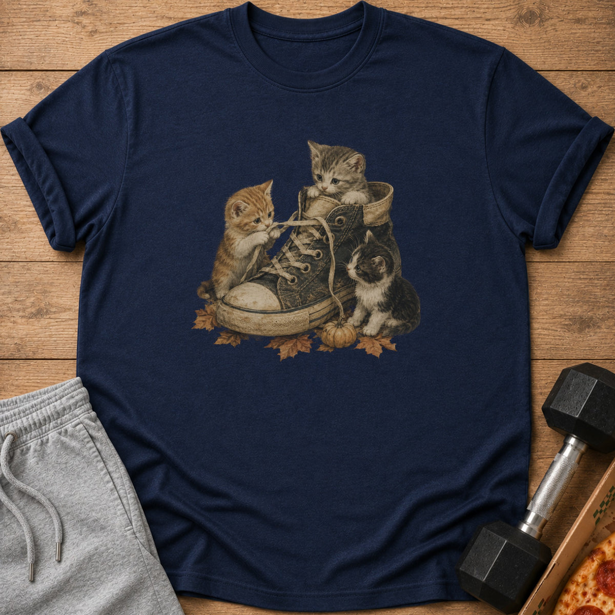 Three kittens play with shoelaces in a worn sneaker surrounded by autumn leaves.