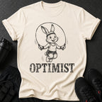 Cream t-shirt with a cartoon bunny jumping rope and the word "OPTIMIST".