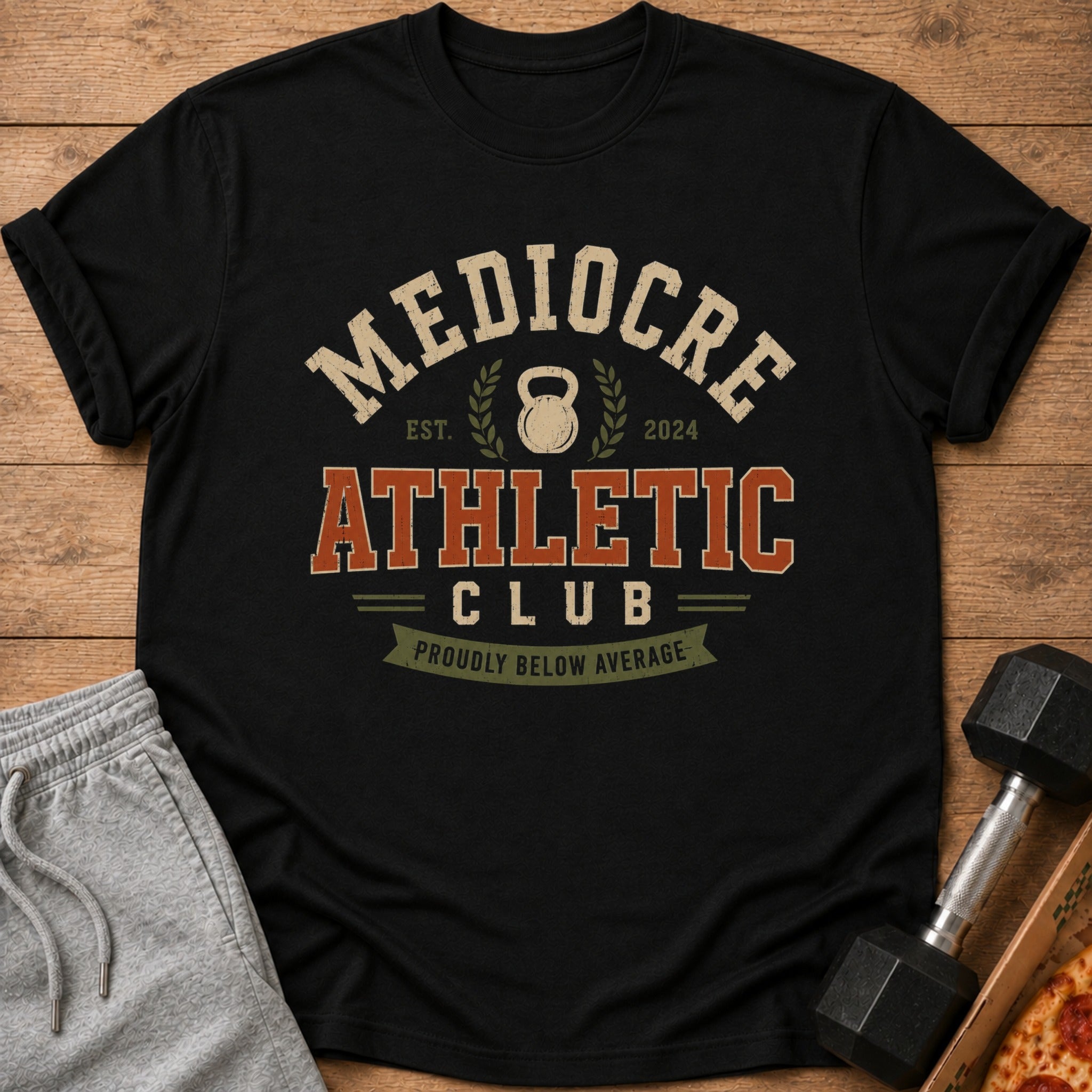 Black t-shirt with "Mediocre Athletic Club" text and "Proudly Below Average" banner.
