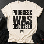 Cream t-shirt with black distressed text "PROGRESS WAS DISCUSSED" and a checklist icon.