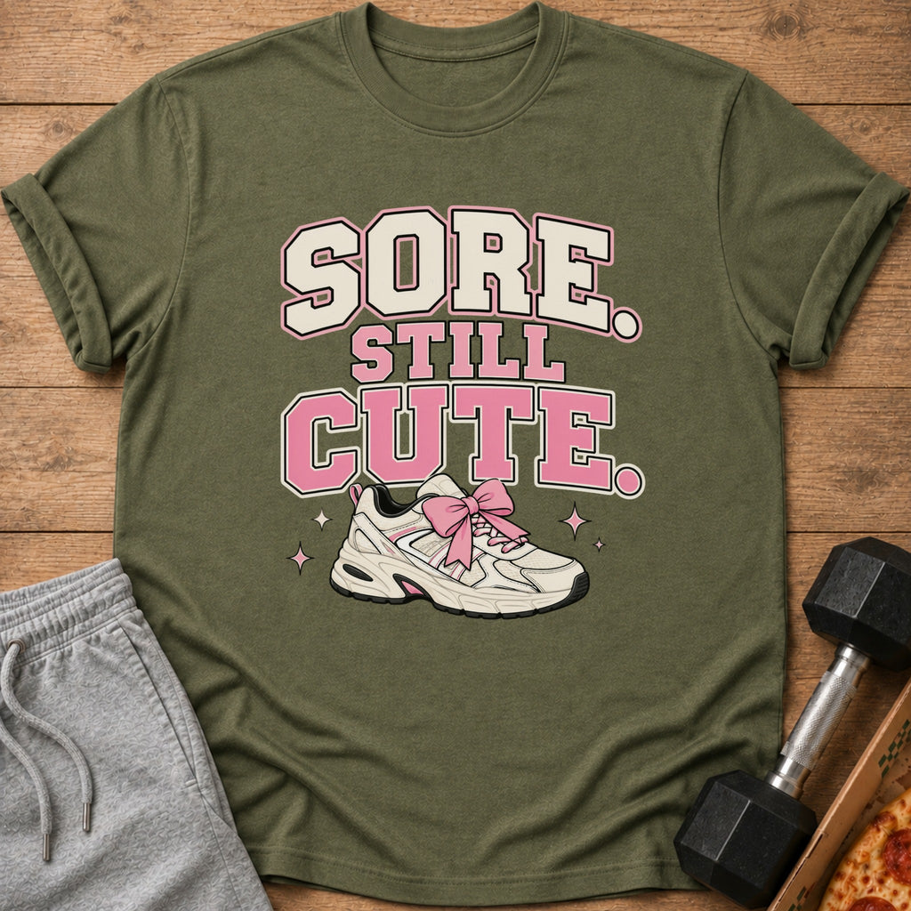 Olive green t-shirt with "SORE STILL CUTE" text and a sneaker with a pink bow.