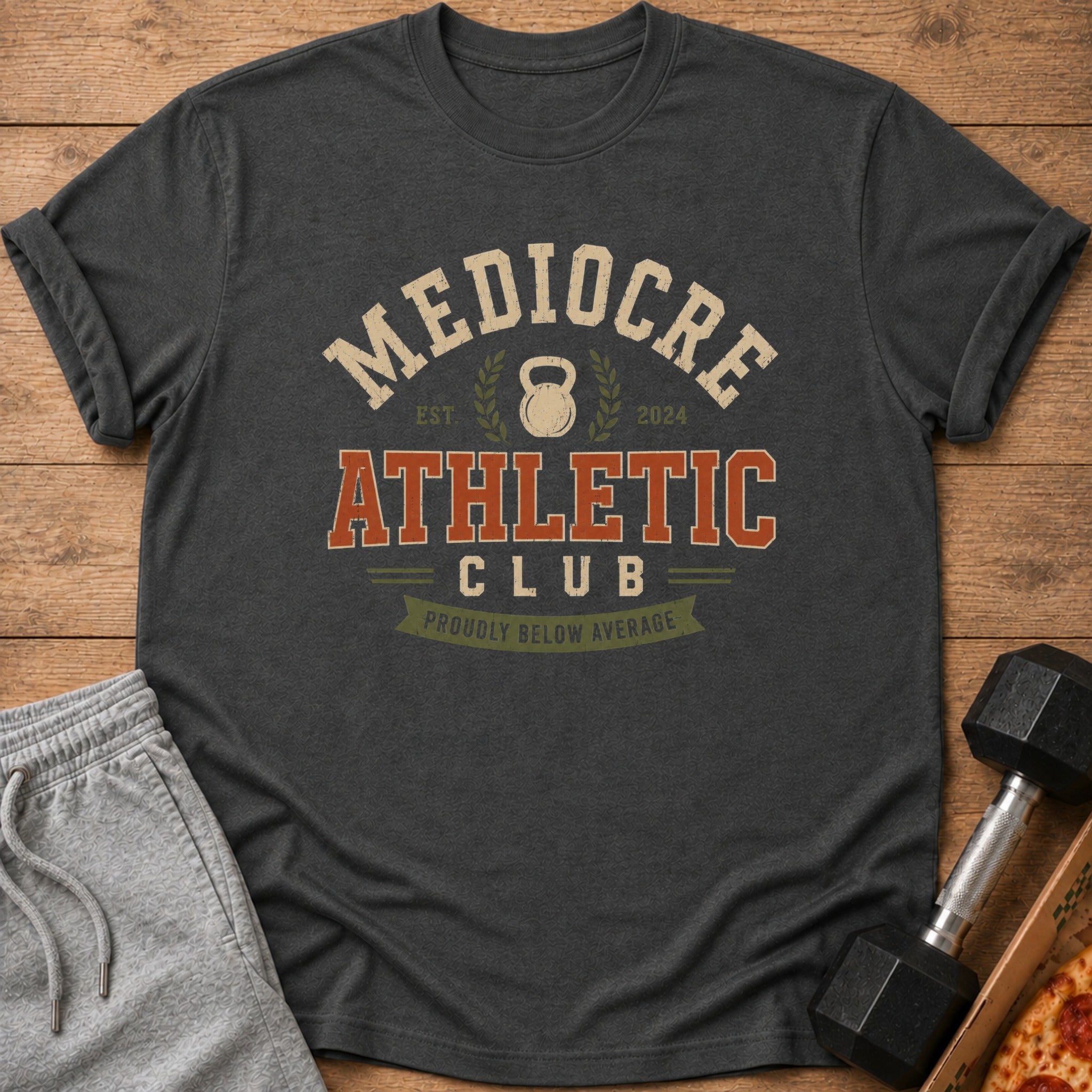 Dark grey t-shirt with "Mediocre Athletic Club" text and kettlebell graphic.