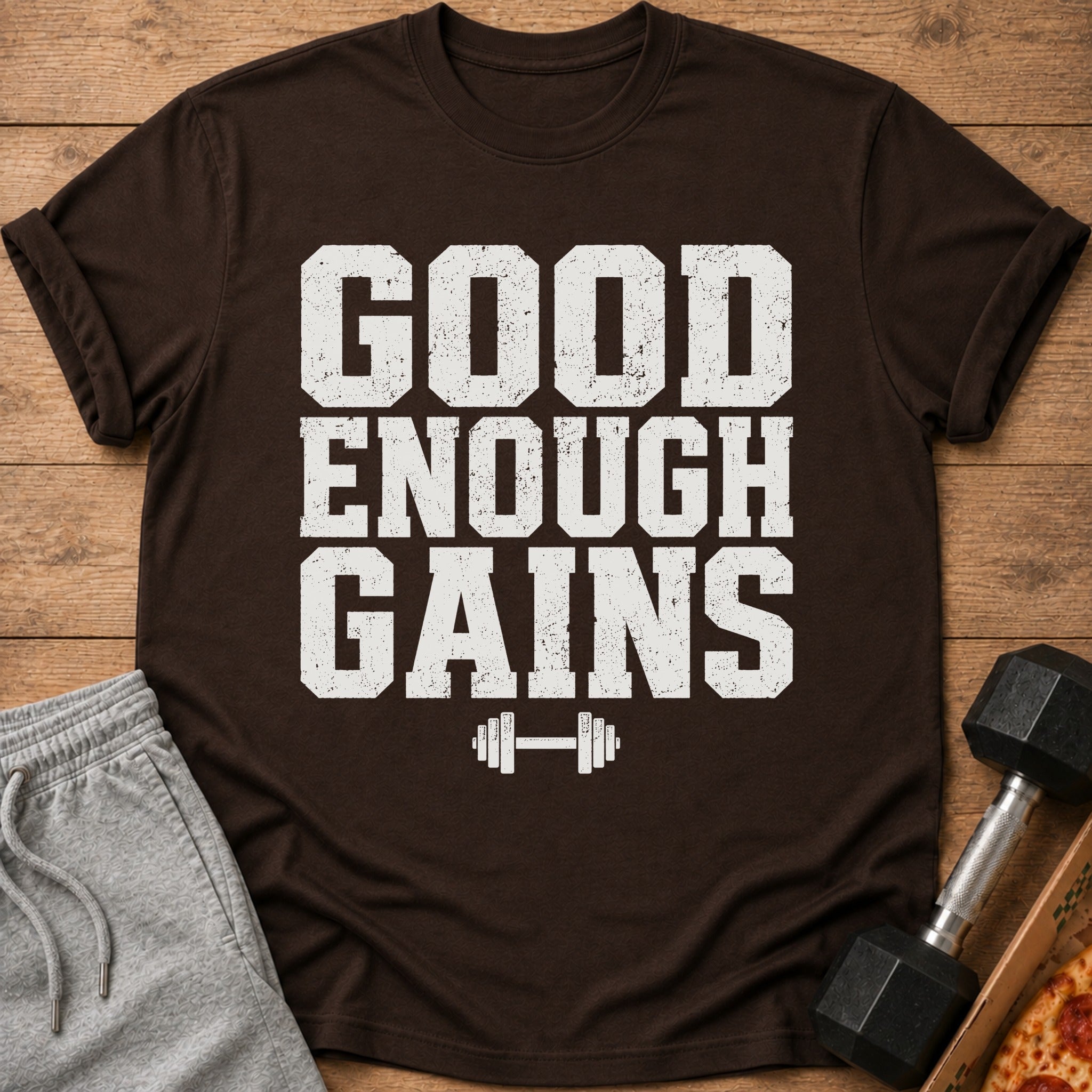 Brown t-shirt with white text "GOOD ENOUGH GAINS" and dumbbell graphic.