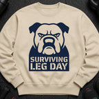 Tan sweatshirt with a navy blue bulldog graphic and "SURVIVING LEG DAY" text.