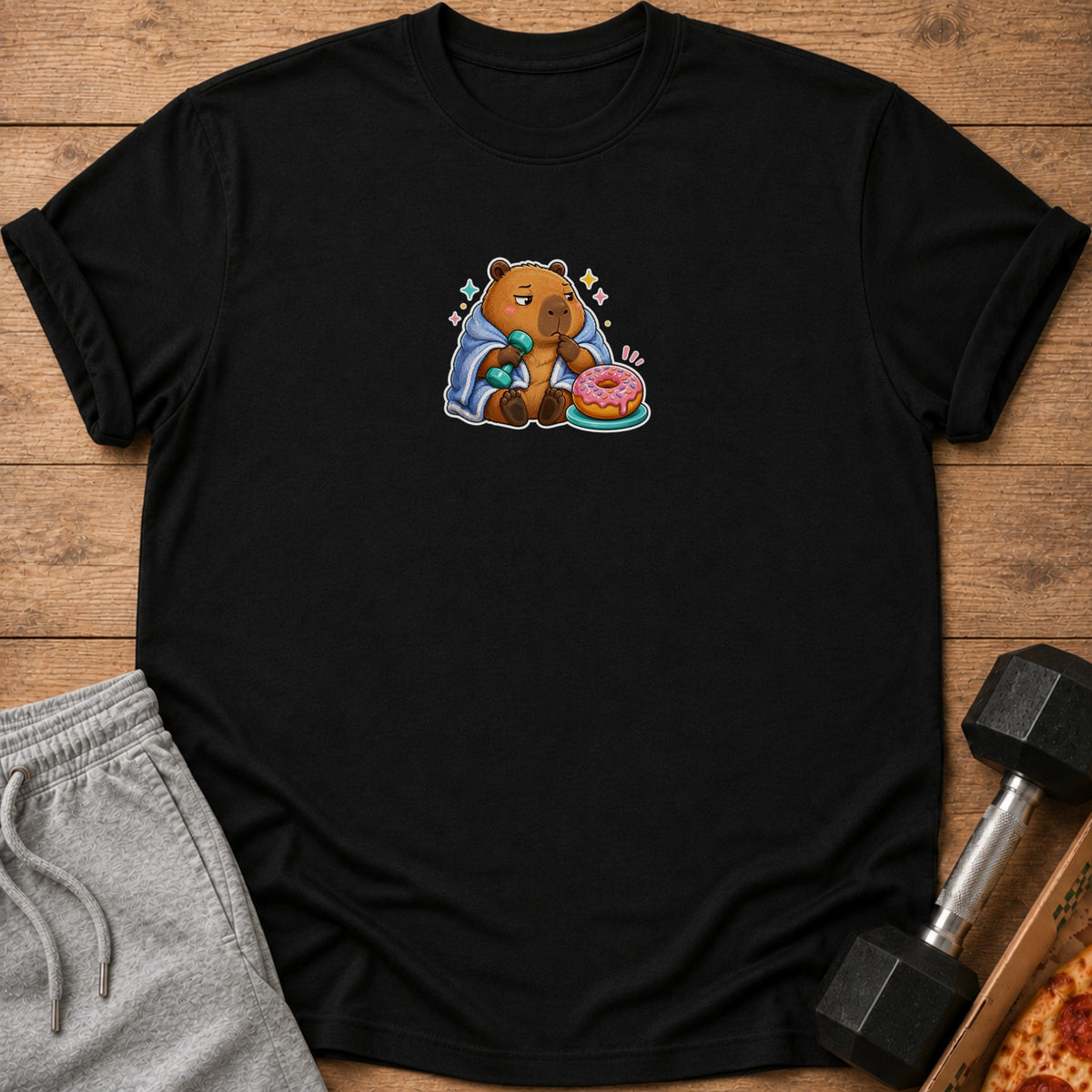 Black t-shirt with a cartoon capybara holding a dumbbell and eating a donut.